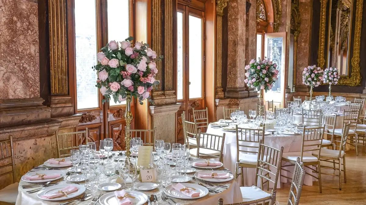 Interior del Salón de los Reyes en el Casino Español con mesas, candelabros y pinturas. Se ven centros de mesas con flores.