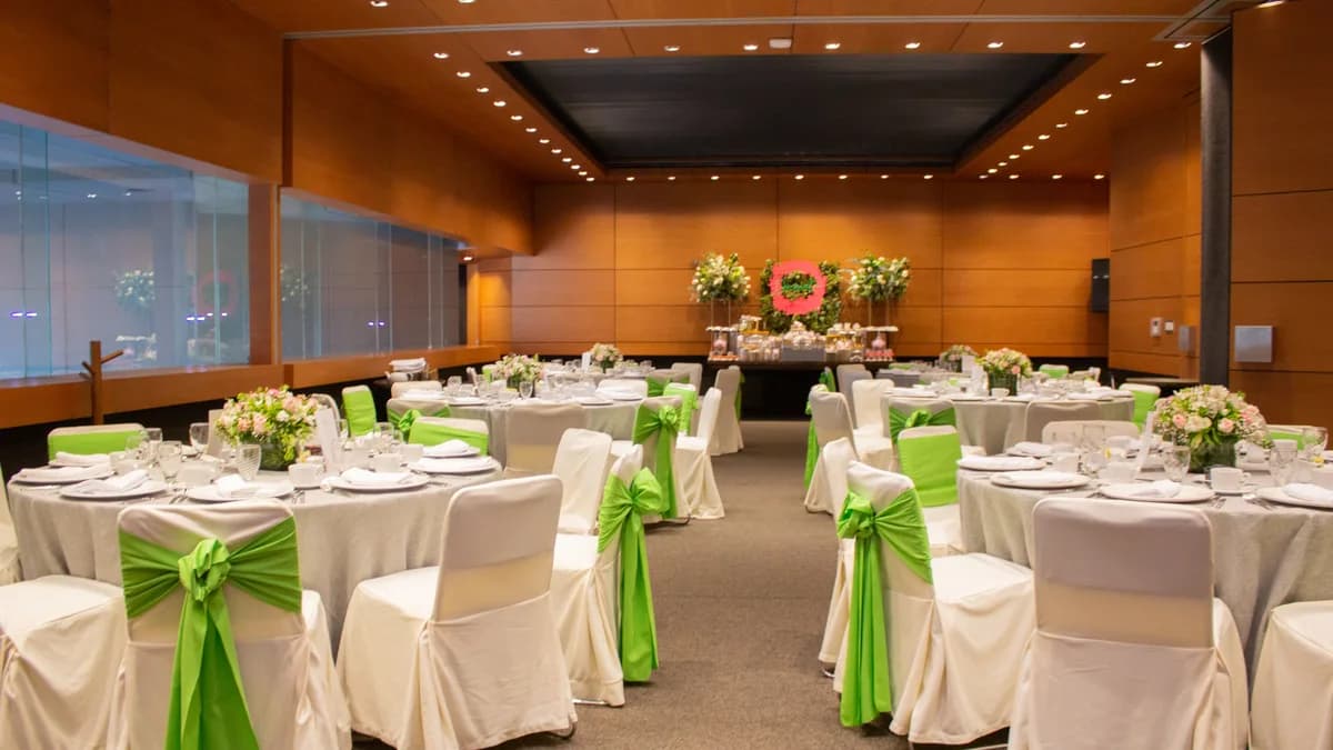 Salón de eventos Purón en el Asturiano Polanco con mesas redondas con tonos verdes en la silla. Hay centro de mesa con flores.